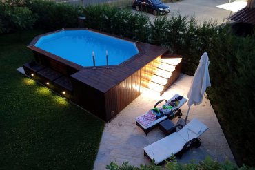 Piscina ottagonale in legno JARDIN 607 in legno scuro, con panca integrata e illuminazione notturna che crea un’atmosfera calda e avvolgente.