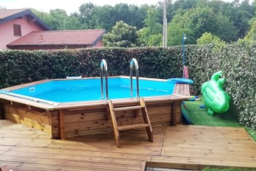 Piscina in legno JARDIN 434 esagonale in legno trattato, completa di decking integrato e siepe verde, perfetta per momenti di relax all’aria aperta.