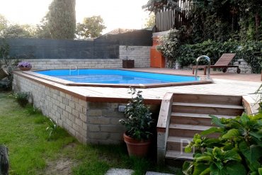 Piscina ottagonale fuori terra da 6,07 m, incorniciata da un ampio solarium con vista collinare. Eleganza e relax in giardino.