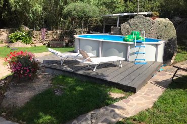 Elegante piscina fuori terra in acciaio White Pool 490x360, installata su piattaforma in legno con vista su roccia e vegetazione. Scala ergonomica, liner resistente e struttura zincata per una durata superiore.